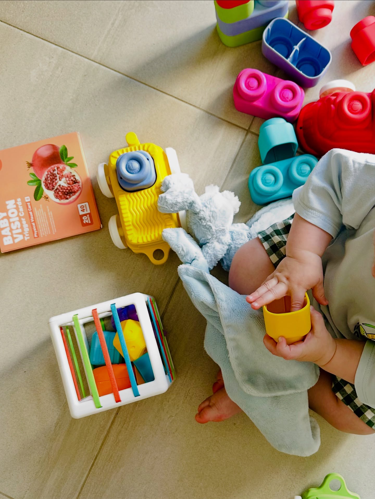 A baby's hands reaching for stacking cups and sensory toys spread across a cool tiled floor