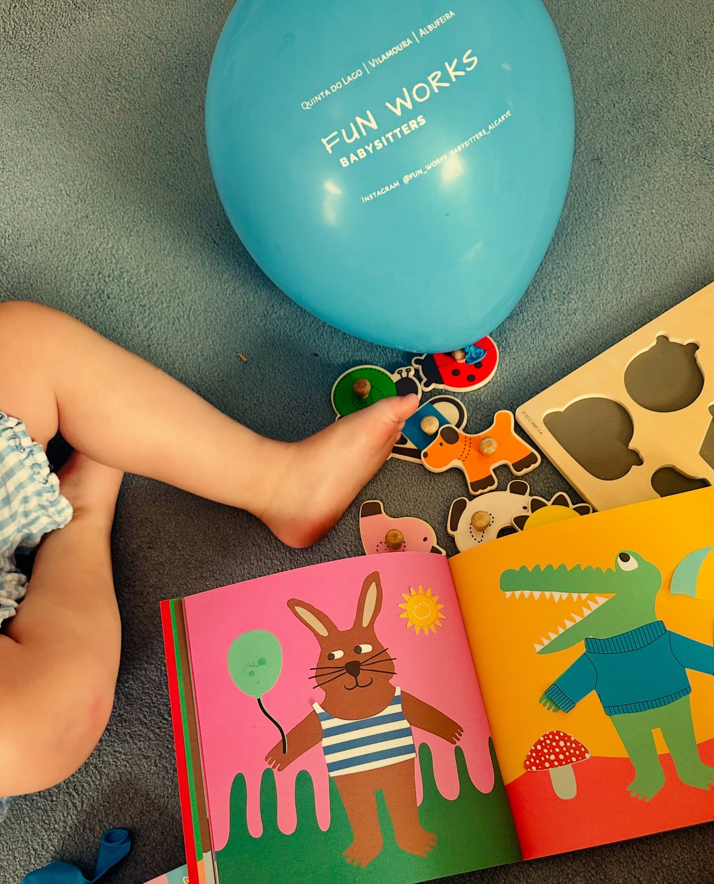 A FunWorks Babysitters balloon printed with Quinta do Lago, Vilamoura and Albufeira, beside a picture book and wooden puzzle pieces
