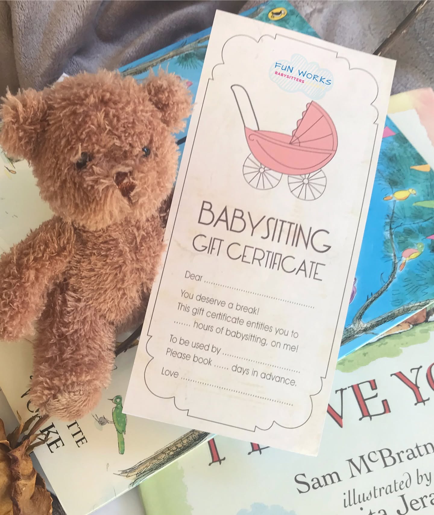 A FunWorks babysitting gift certificate resting on a stack of picture books with a small teddy bear